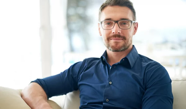 Man sitting on couch, wearing a pair of prescription eyeglasses.