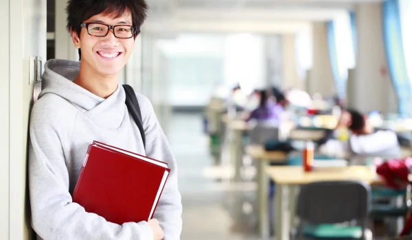 Young student leaning on wall, wearing prescription eyeglasses.